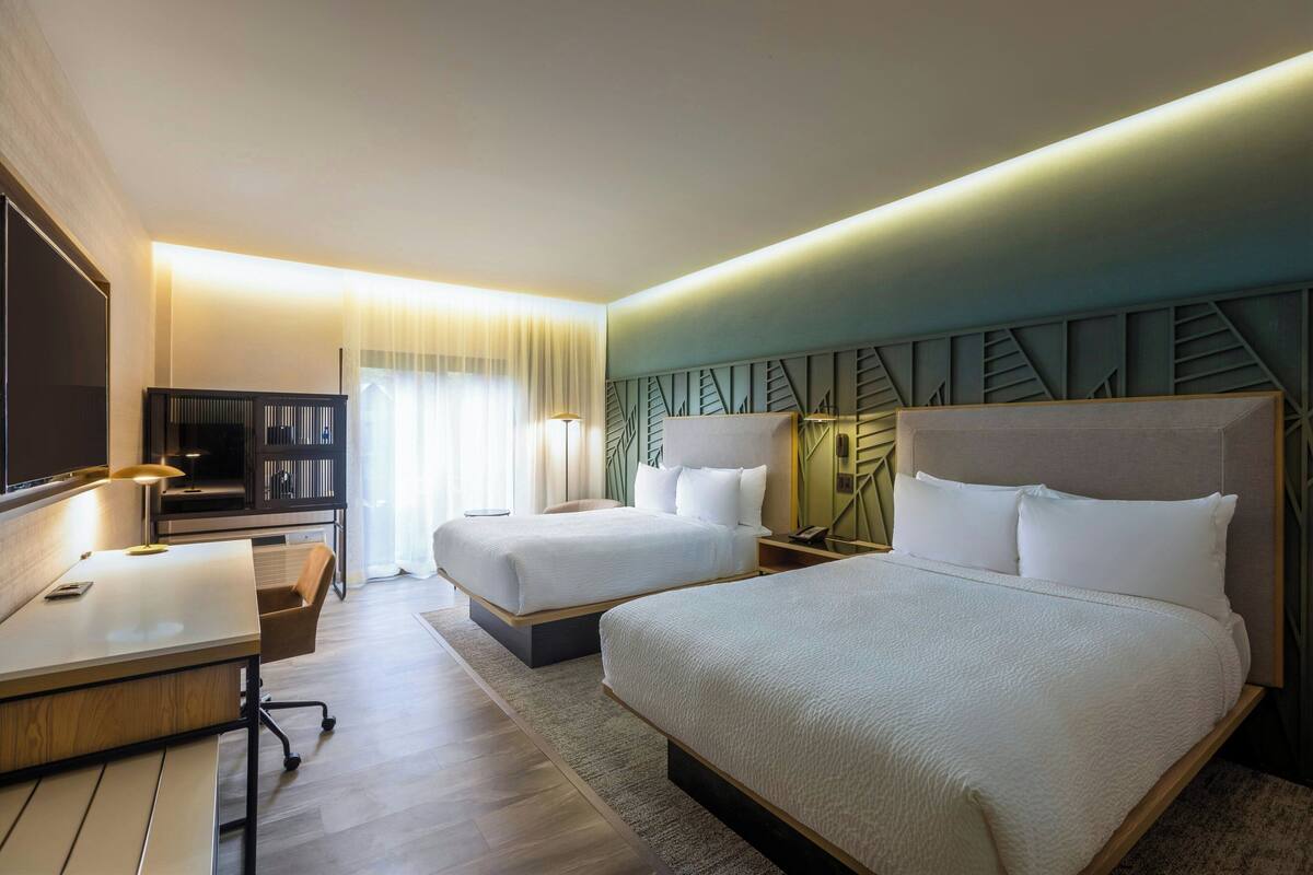 Een hotelkamer met twee bedden, een bureau, een televisie en een groot raam met gordijnen.