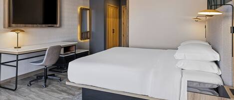 A modern hotel room with a large bed, a desk with a chair, a flat-screen TV, and a mirror.