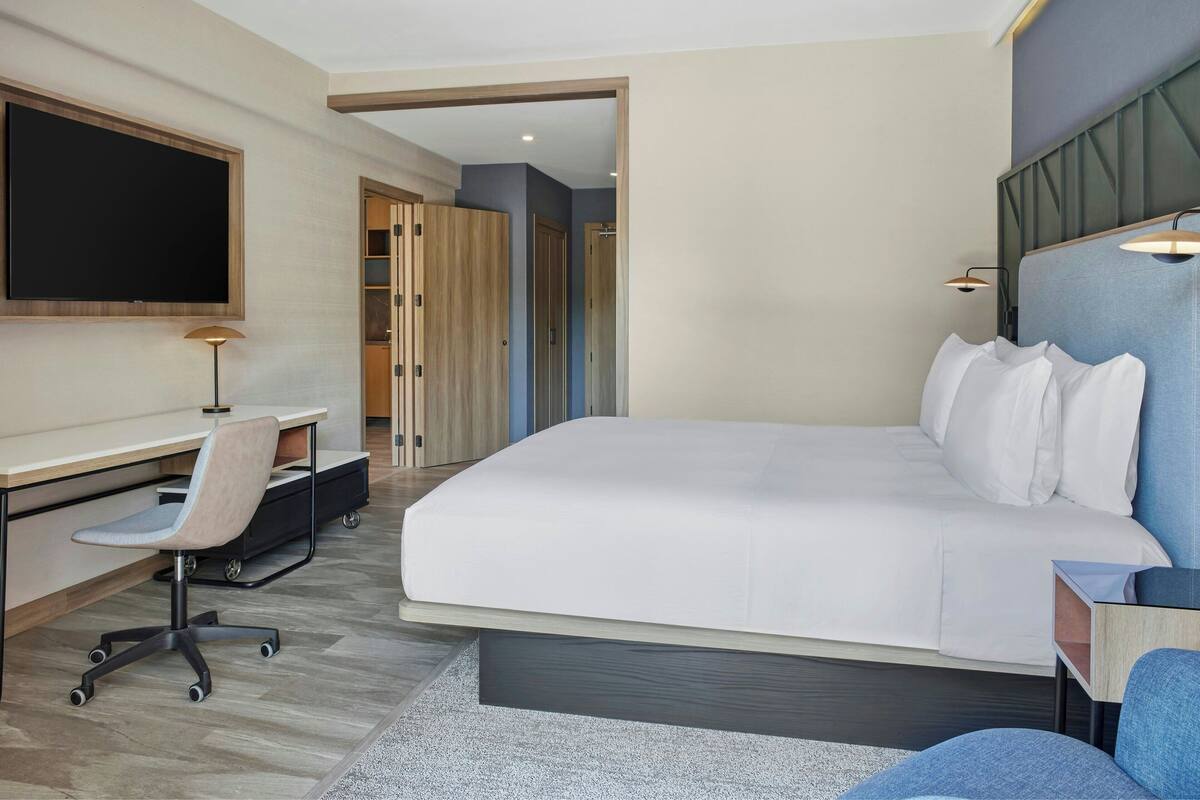 Een moderne hotelkamer met een groot bed, een bureau met stoel, een flatscreen televisie en een kledingkast.