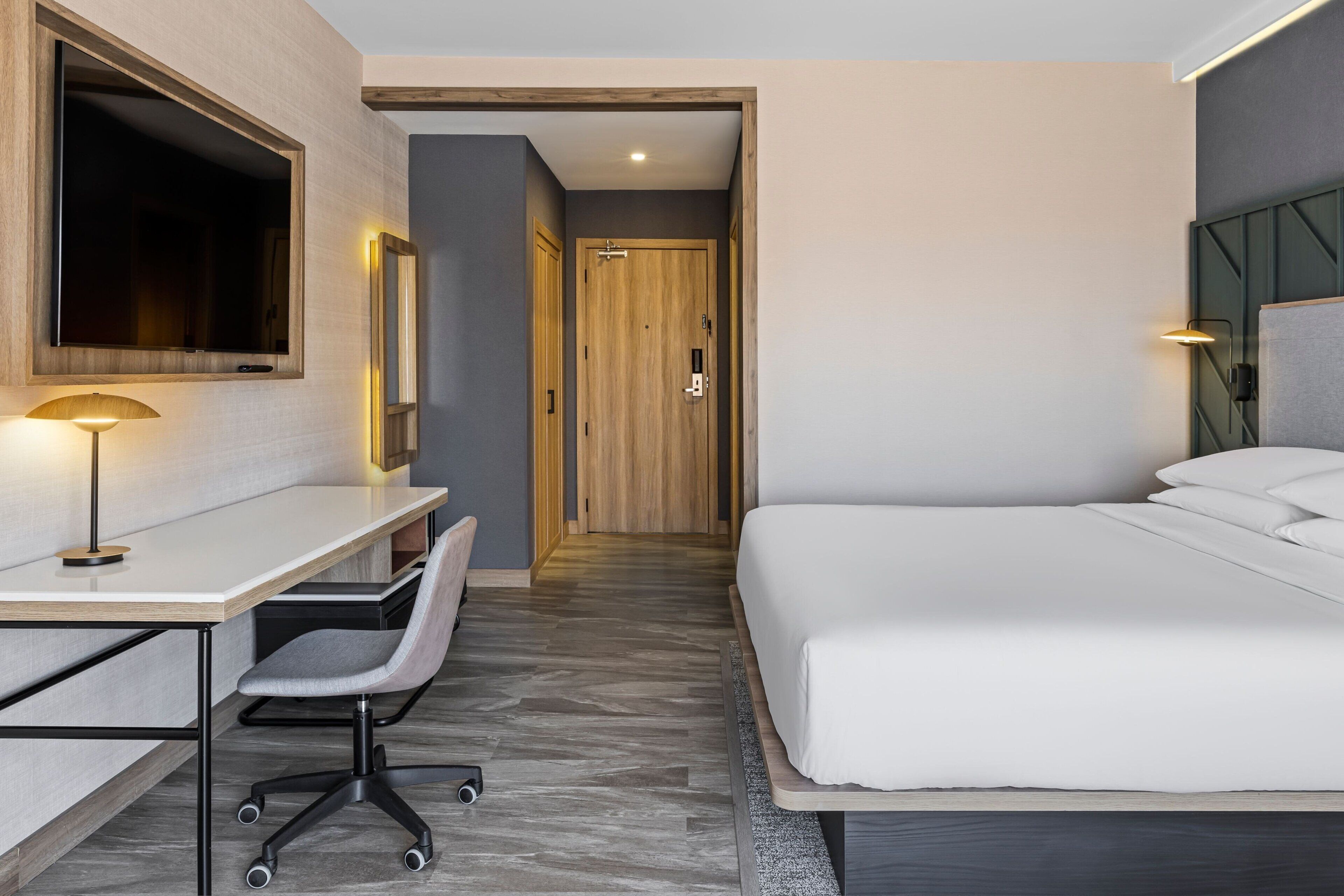 A hotel room with a bed, desk, chair, and a TV.