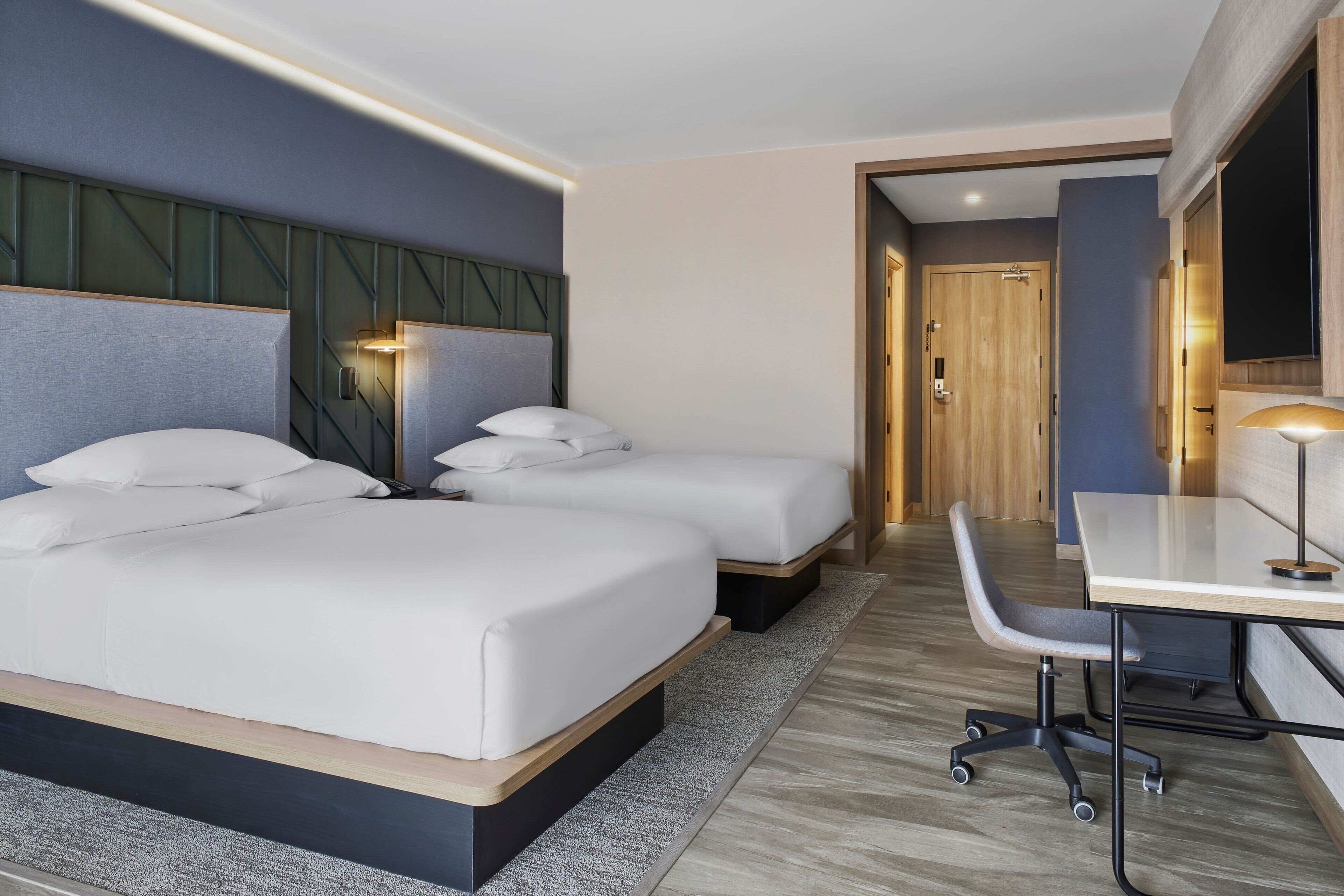 A modern hotel room with a large bed, a desk, and a chair.