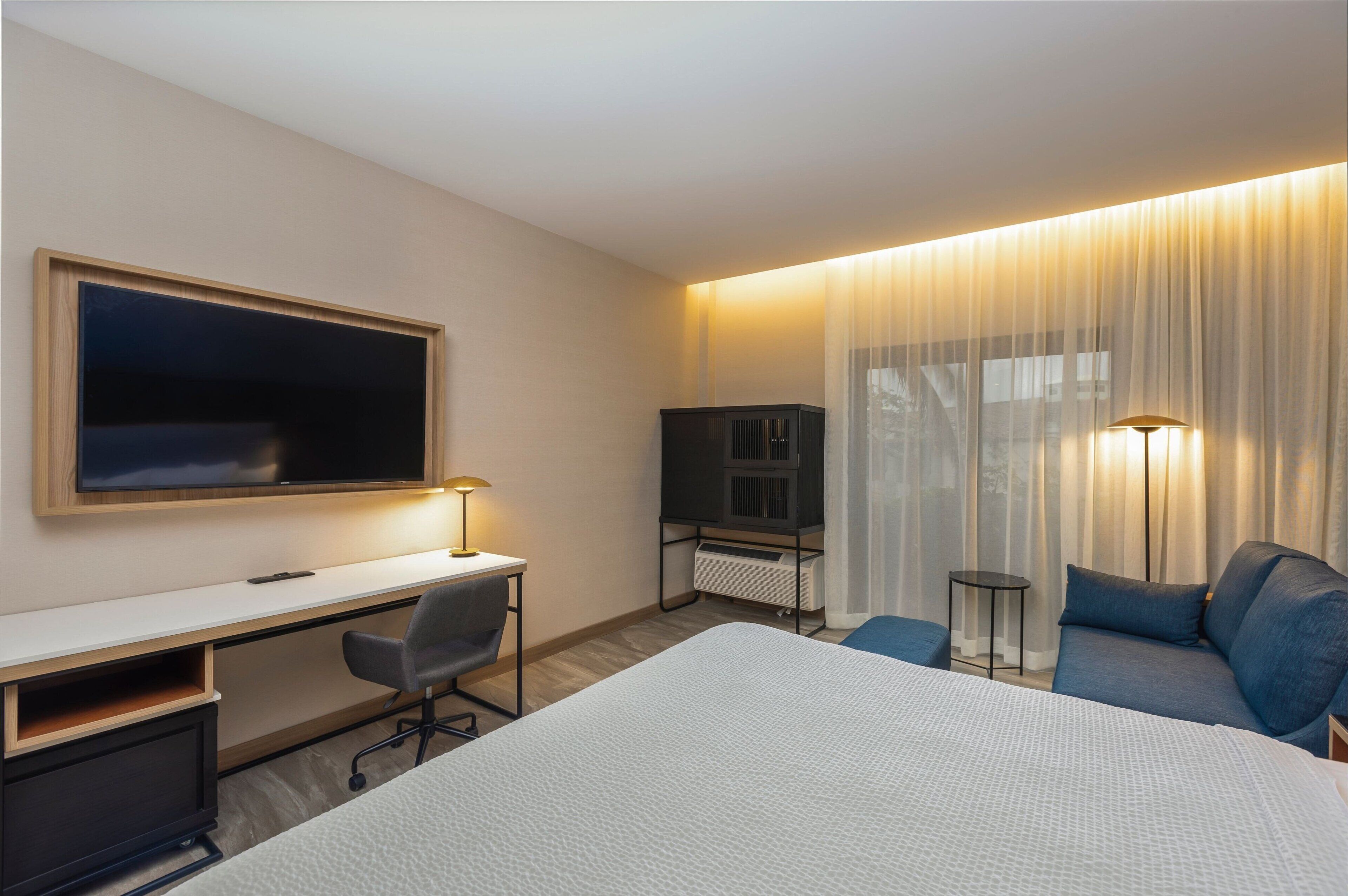 Une chambre d’hôtel équipée d’un lit, d’un bureau, d’une chaise, d’une télévision, d’une lampe et d’un canapé.