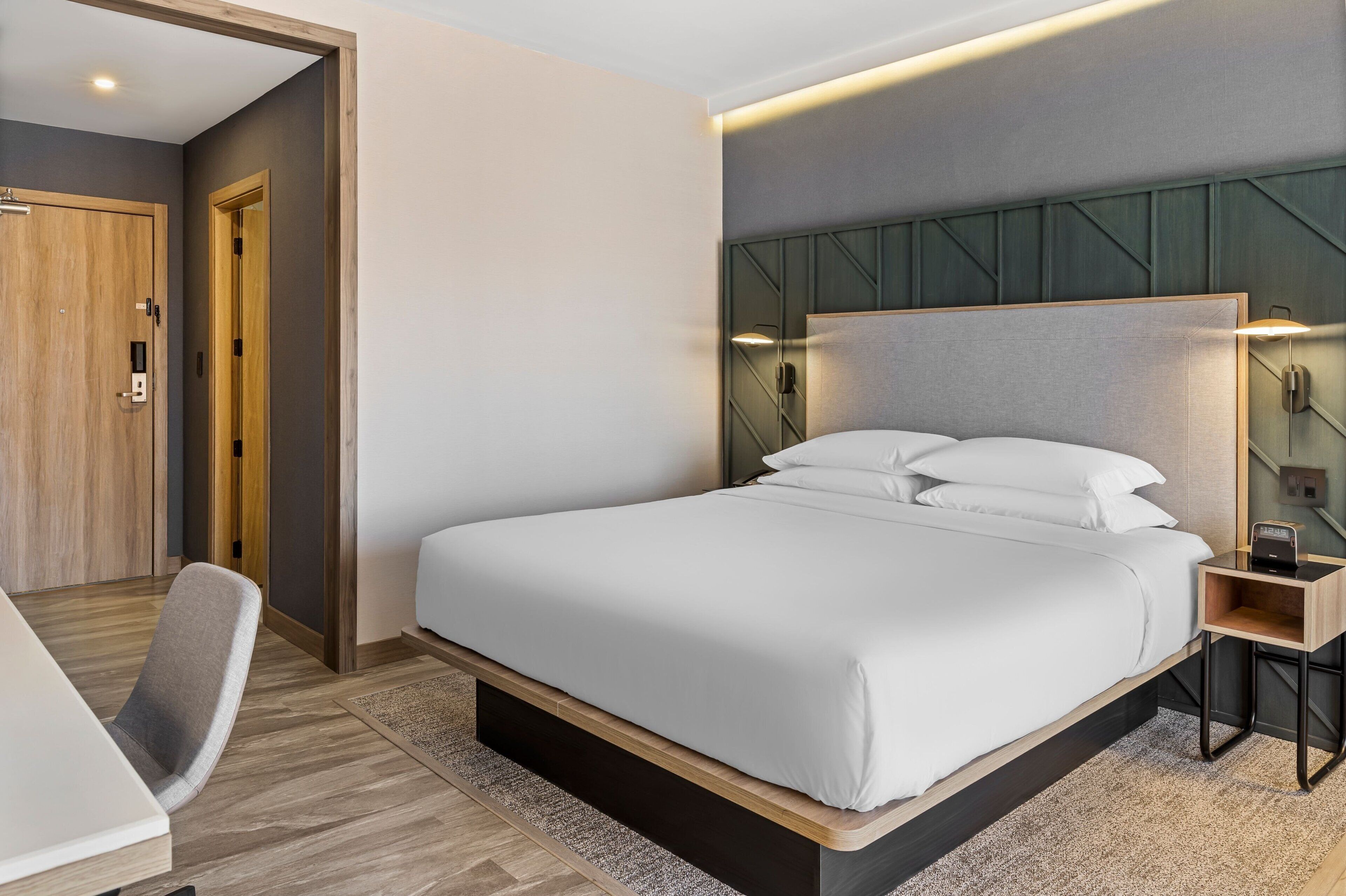 A modern hotel room with a large bed, a desk, and a chair.