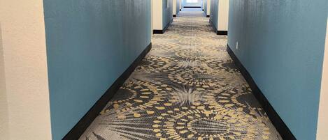 A hotel hallway with blue walls, a patterned carpet, and a tiled ceiling.