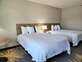 Habitación de hotel con dos camas, cabecera de madera, lámpara de noche y alfombra estampada.