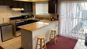 A modern kitchen with a central island, dark cabinets, a built-in oven, and a window with blinds. - Days Inn by Wyndham Newport OR (Newport)