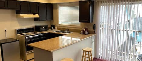 Una cocina moderna con una isla central, armarios oscuros, horno empotrado y ventana con persianas.