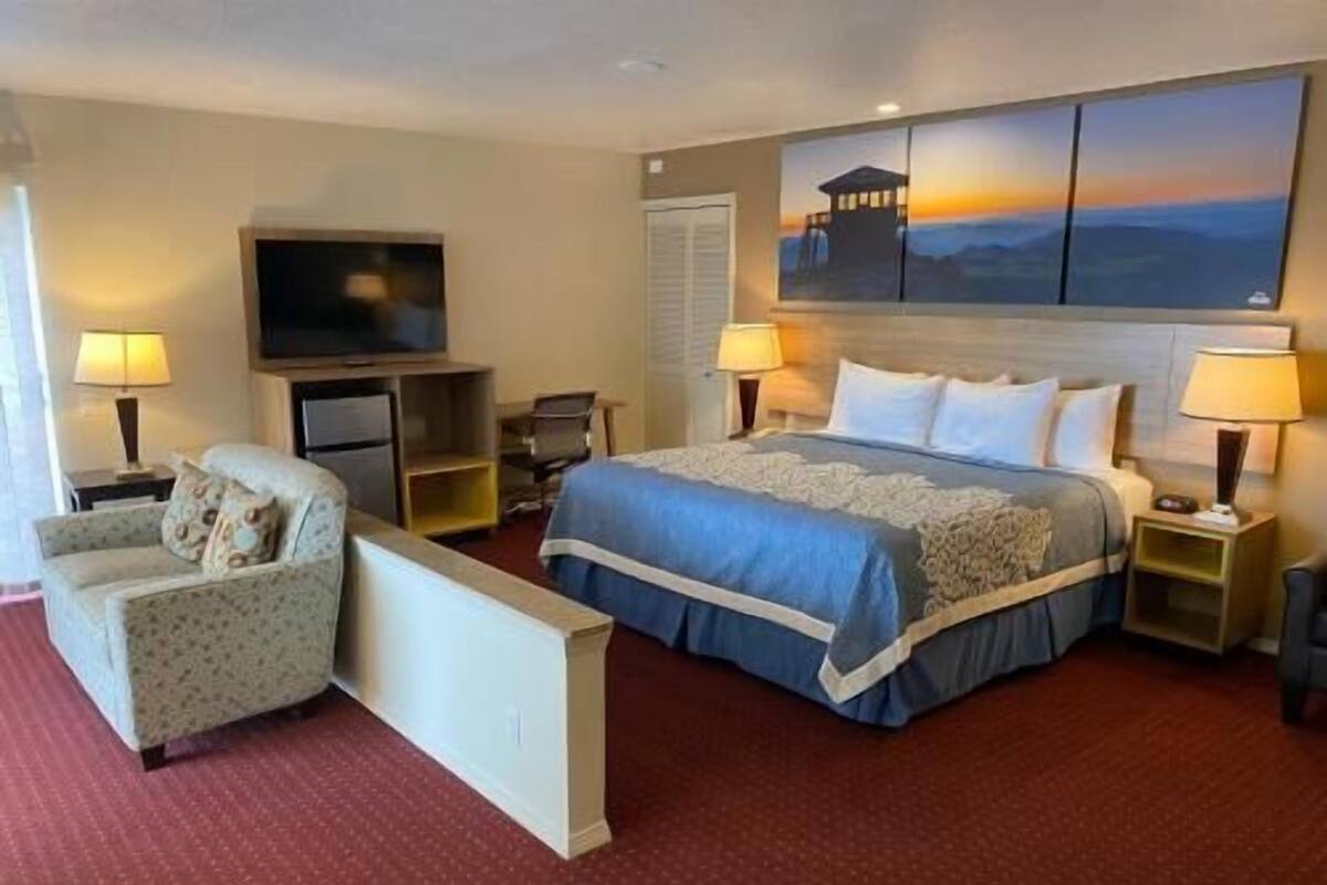 A hotel room with a bed, two bedside tables, a TV, a chair, and a painting on the wall.