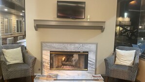A cozy lounge area with a fireplace, two patterned armchairs, and a flat-screen TV mounted above the mantel. - Days Inn by Wyndham Newport OR (Newport)