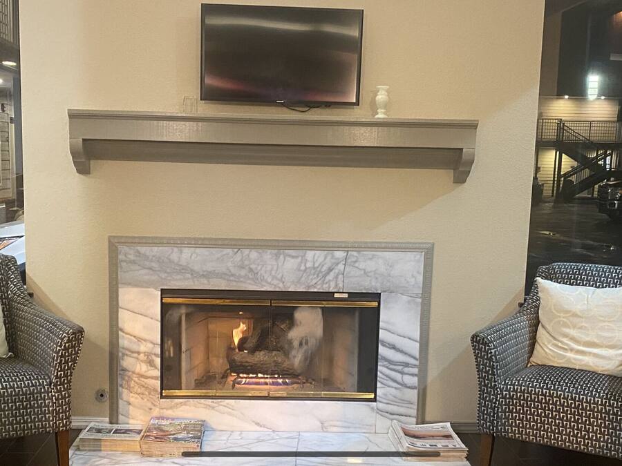 A cozy lounge area with a fireplace, two patterned armchairs, and a flat-screen TV mounted above the mantel.