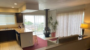 A modern kitchen with a central island, a dining area with a sofa and a lamp, and a large window with blinds. - Days Inn by Wyndham Newport OR (Newport)