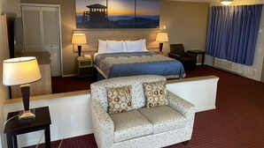 A hotel room with a king-sized bed, two bedside tables with lamps, a sofa, a large window with curtains, and a wall-mounted artwork depicting a mountain scene. - Days Inn by Wyndham Newport OR (Newport)