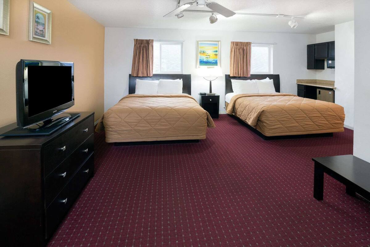 A hotel room with two beds, a TV, a desk, and a ceiling fan.