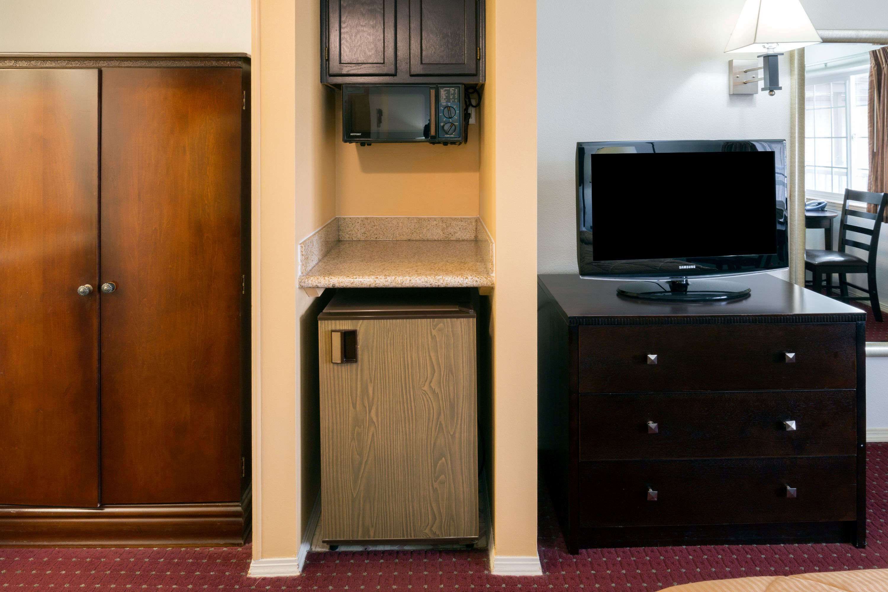A compact hotel room with a wardrobe, a microwave, a television, and a small refrigerator.