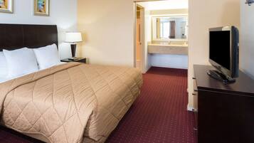 A hotel room with a bed, a TV, a nightstand, a lamp, and a bathroom visible through an open door.