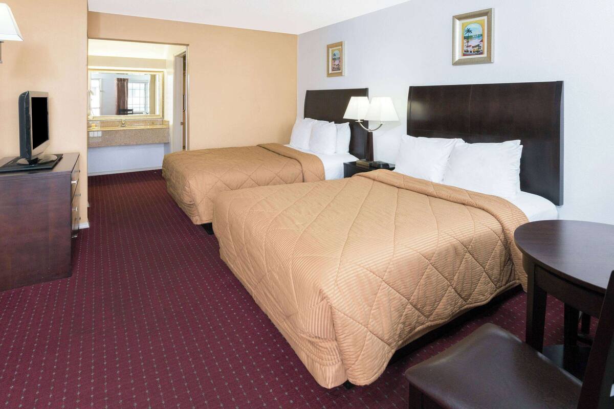 A hotel room with two beds, a desk with a computer, a chair, a small table, a mirror, and a picture on the wall.