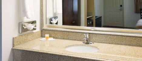 A bathroom with a granite countertop sink, a mirror, a towel rack, and a door.