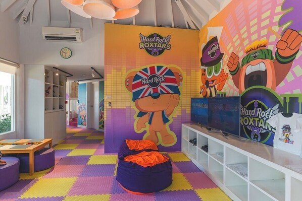 Un salón infantil con piso colorido, un gran mural de Hard Rock ROXTAR y un sillón de peluche.