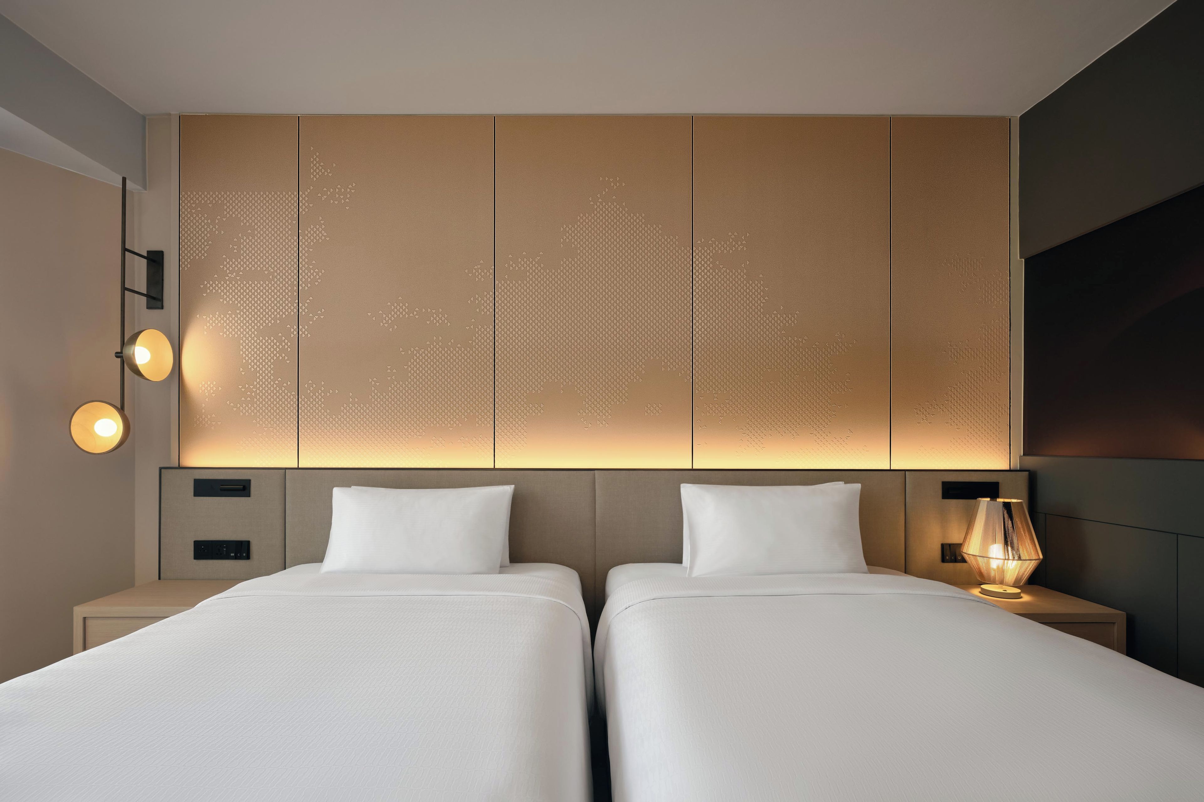 Een hotelkamer met twee bedden, een wandpaneel met een geometrisch patroon, bedlampen en een nachtkastje met een lamp.