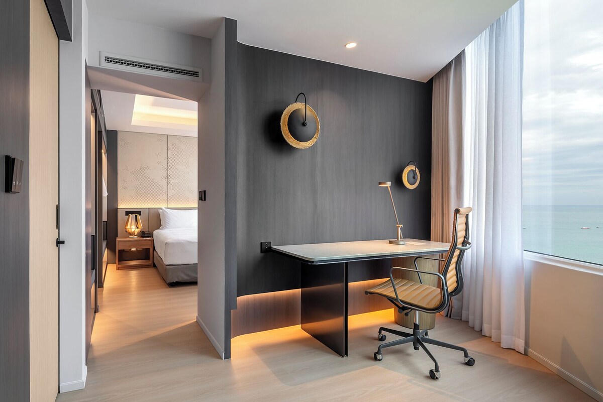 A modern hotel room with a desk, chair, and a view of the sea.