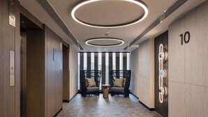 A modern hallway with two black chairs, a small wooden table, and a circular light fixture on the ceiling.