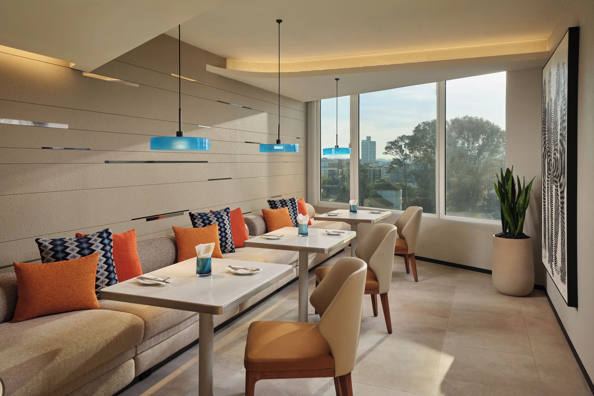 Un comedor moderno con una mesa larga, asientos acolchados, iluminación colgante y un gran ventanal con vistas a la ciudad.