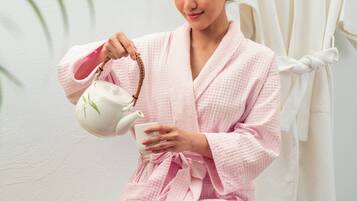 Una persona vestida con bata sentada en un banco, sosteniendo una tetera y una taza.