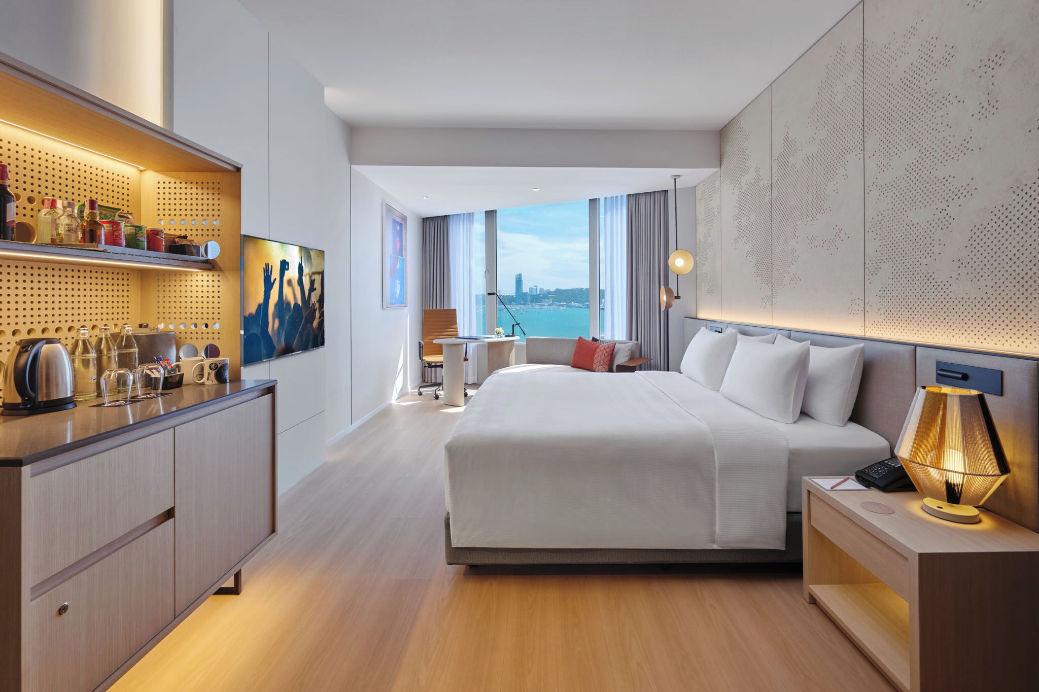 A modern hotel room with a large bed, a desk, a chair, a view of the city, and a wall with a map design.