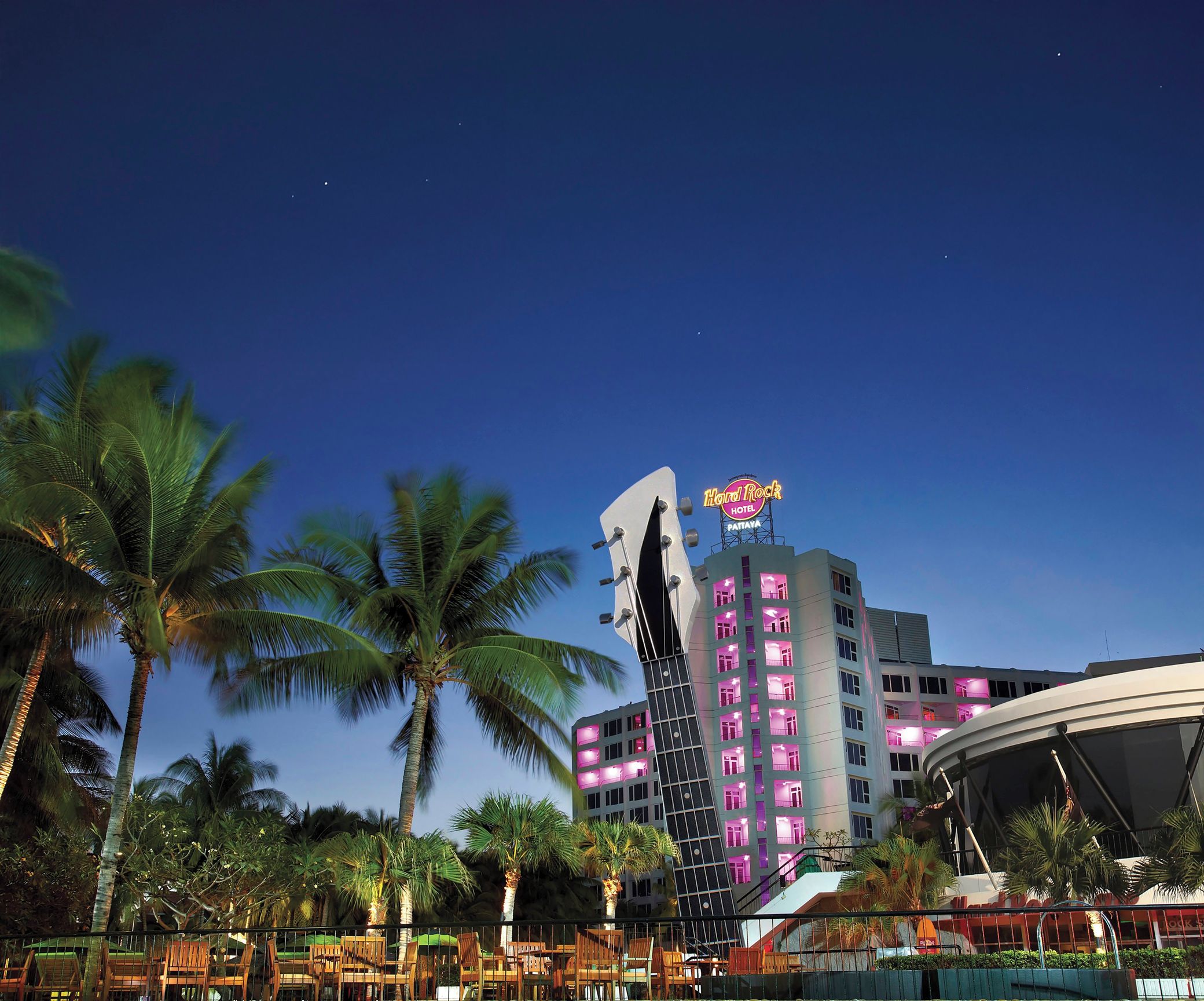 Um hotel com um edifício em formato de guitarra, palmeiras e céu noturno claro.