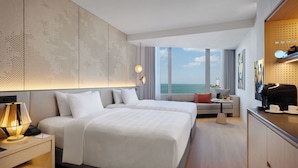 Een moderne hotelkamer met een groot bed, een bureau met lamp, een bijzettafeltje en uitzicht op de oceaan.