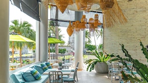 Een terras met een bank, stoelen en parasols, omgeven door potplanten en uitzicht op palmbomen.