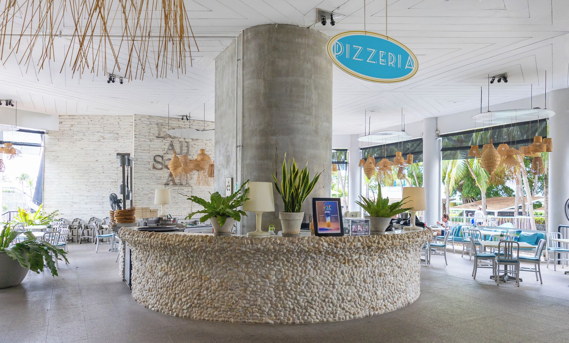 A reception area with a stone counter, potted plants, and a sign reading 'PIZZERIA'.
