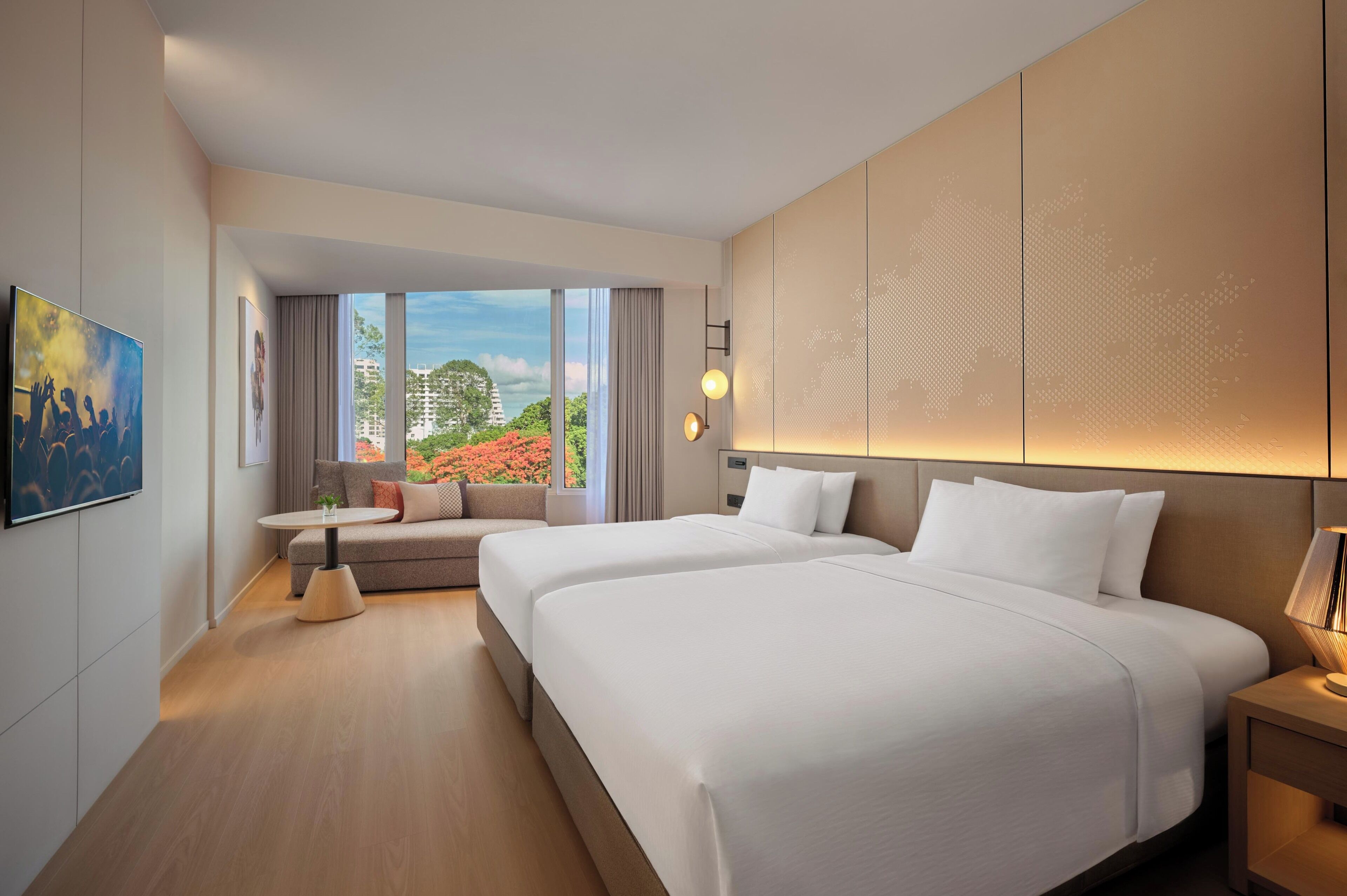 Een hotelkamer met twee bedden, een slaapbank, een televisie en een groot raam met uitzicht op gebouwen en bomen.