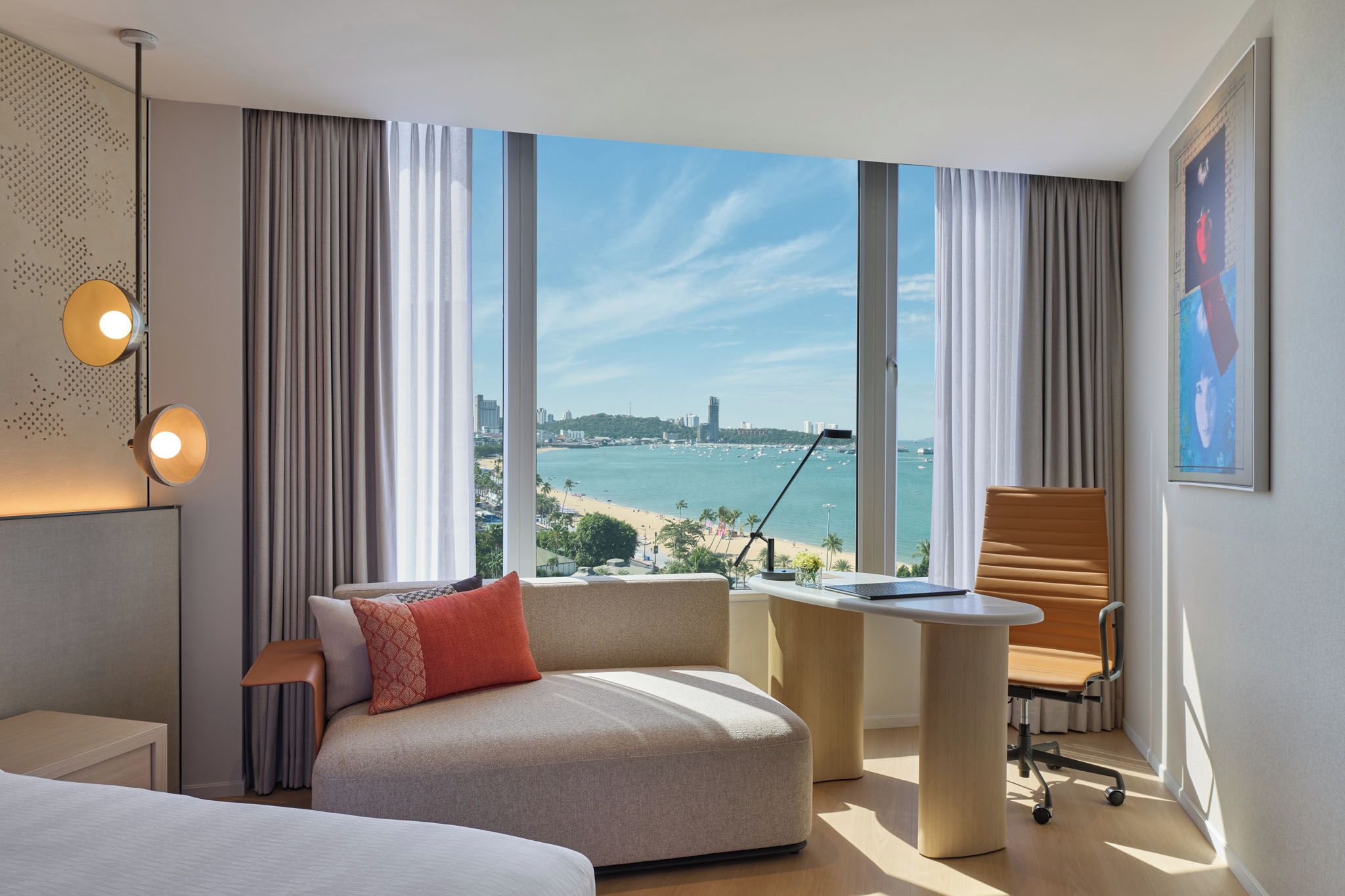 A hotel room with a large window, a bed, a desk, and a chair.