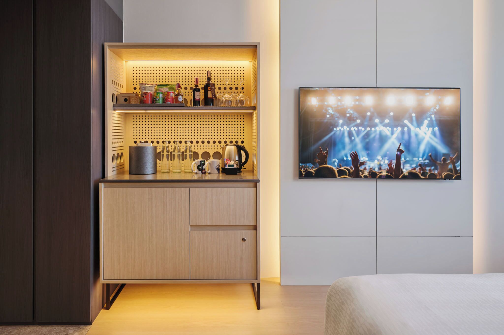 A modern hotel room with a built-in minibar, a flat-screen TV on the wall, and a bed.