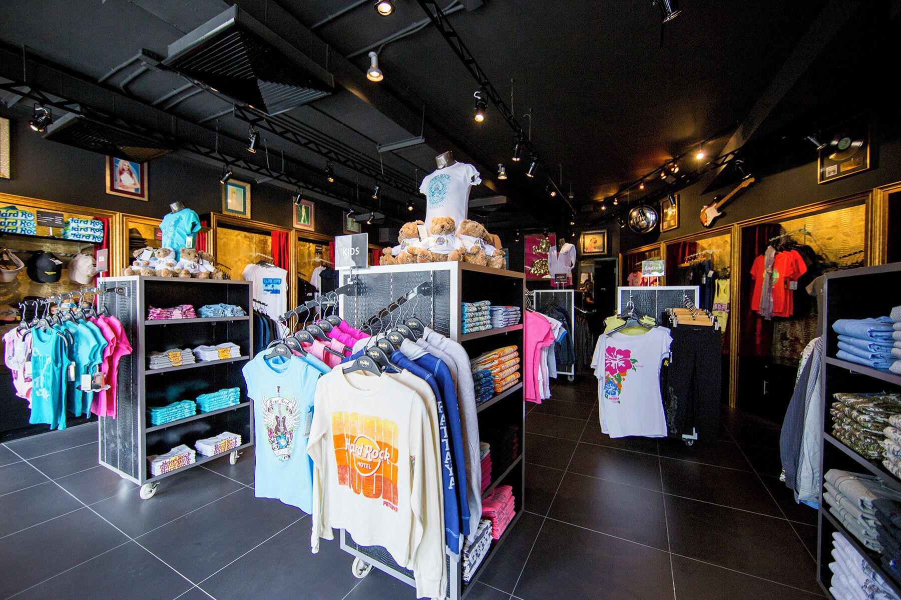 A clothing store with racks of clothes, a teddy bear display, and a sign indicating a kids section.