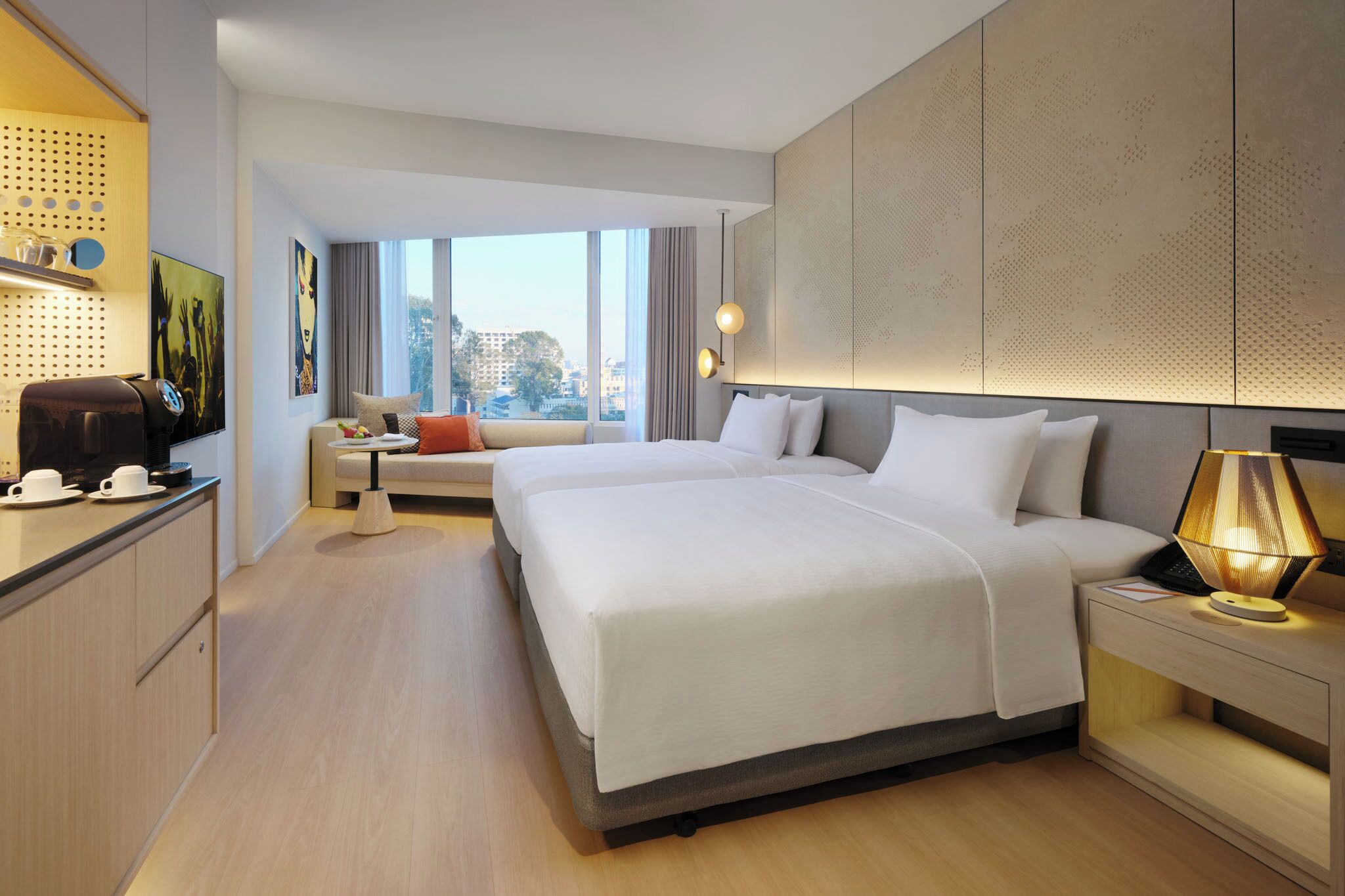 Una camera d'hotel moderna con un letto grande, una scrivania con macchina del caffè, un divano e vista sulla città.