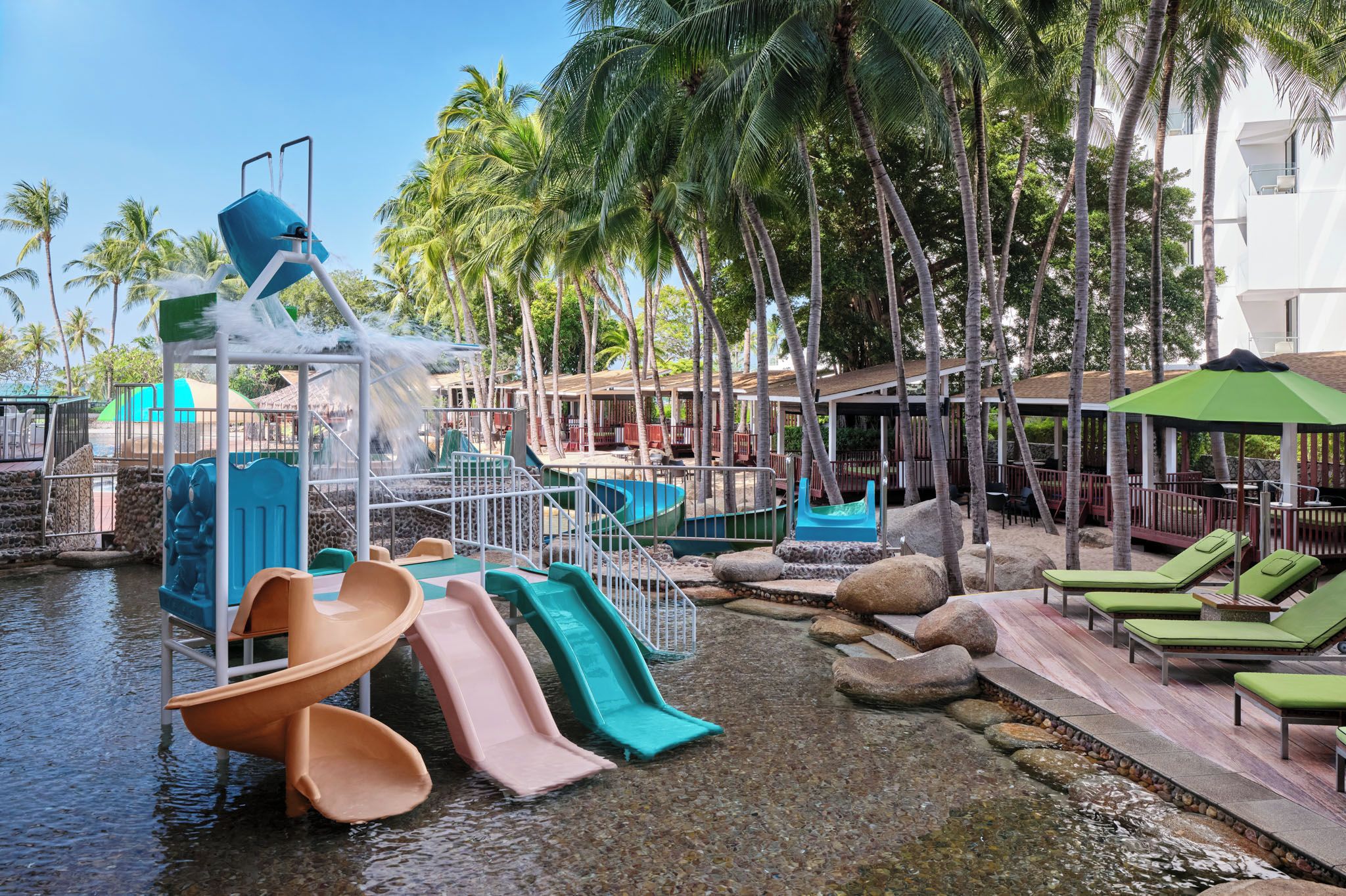 A water park with slides and a pool area, surrounded by palm trees and lounge chairs.