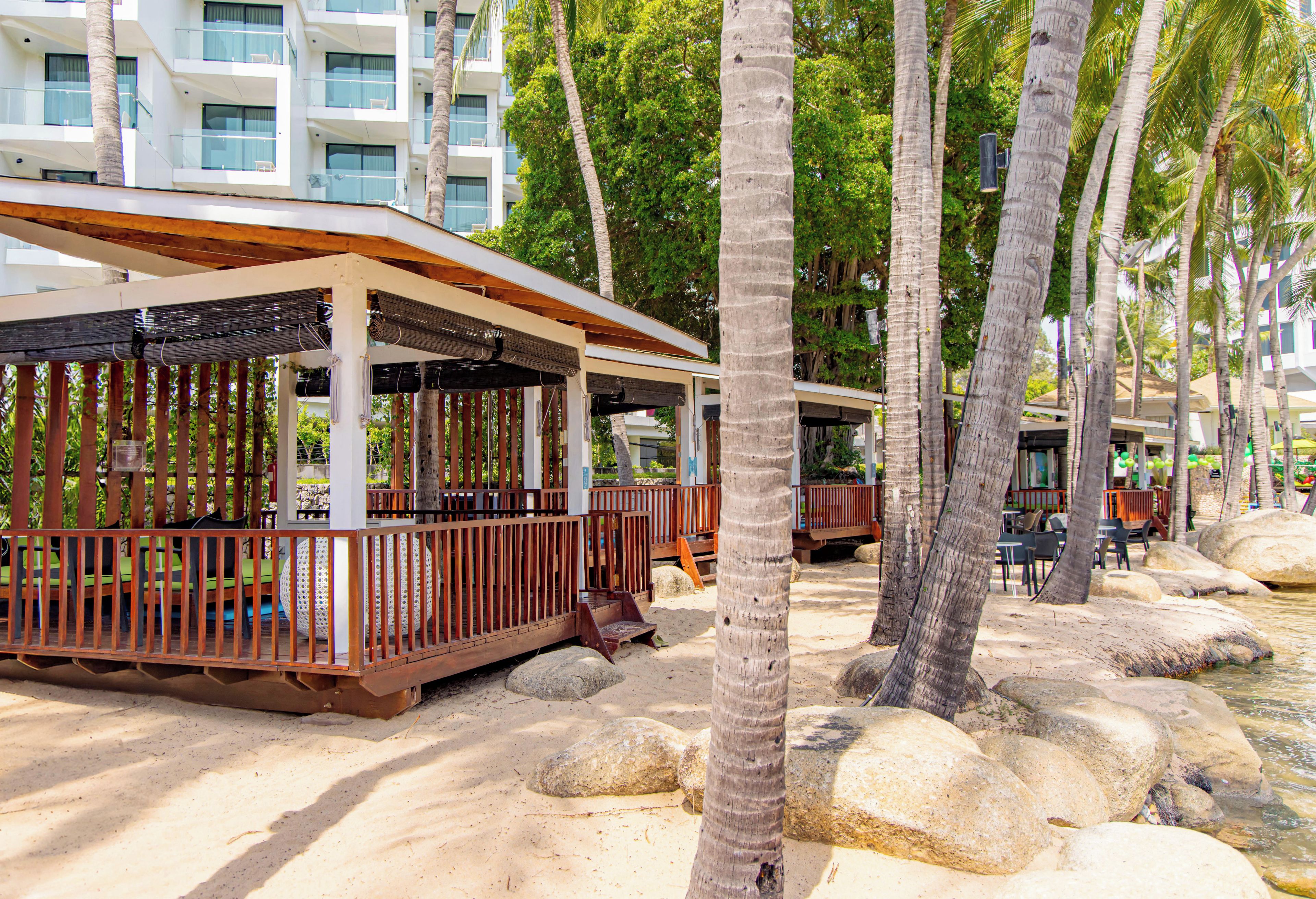 A beachfront resort with wooden cabanas, palm trees, and a sandy beach.