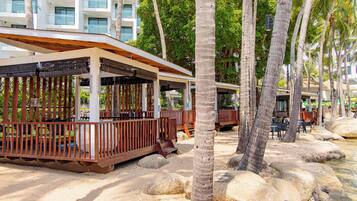 A beachfront resort with wooden cabanas, palm trees, and a sandy beach.