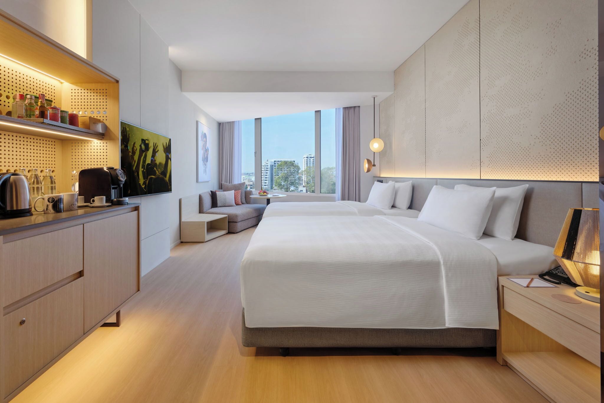 A modern hotel room with a large bed, a desk with a coffee machine, a TV, and a city view.