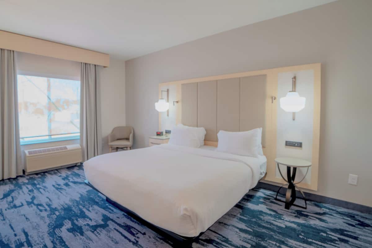 A hotel room with a large bed, a chair, a desk, and a window with curtains.