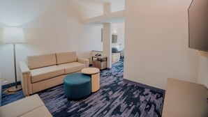 Una habitación de hotel con sofá, reposapiés, lámpara, escritorio y televisor.