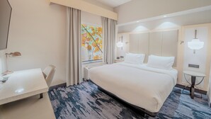 Habitación de hotel con una cama grande, un escritorio, una silla, una mesita y una ventana con cortinas.