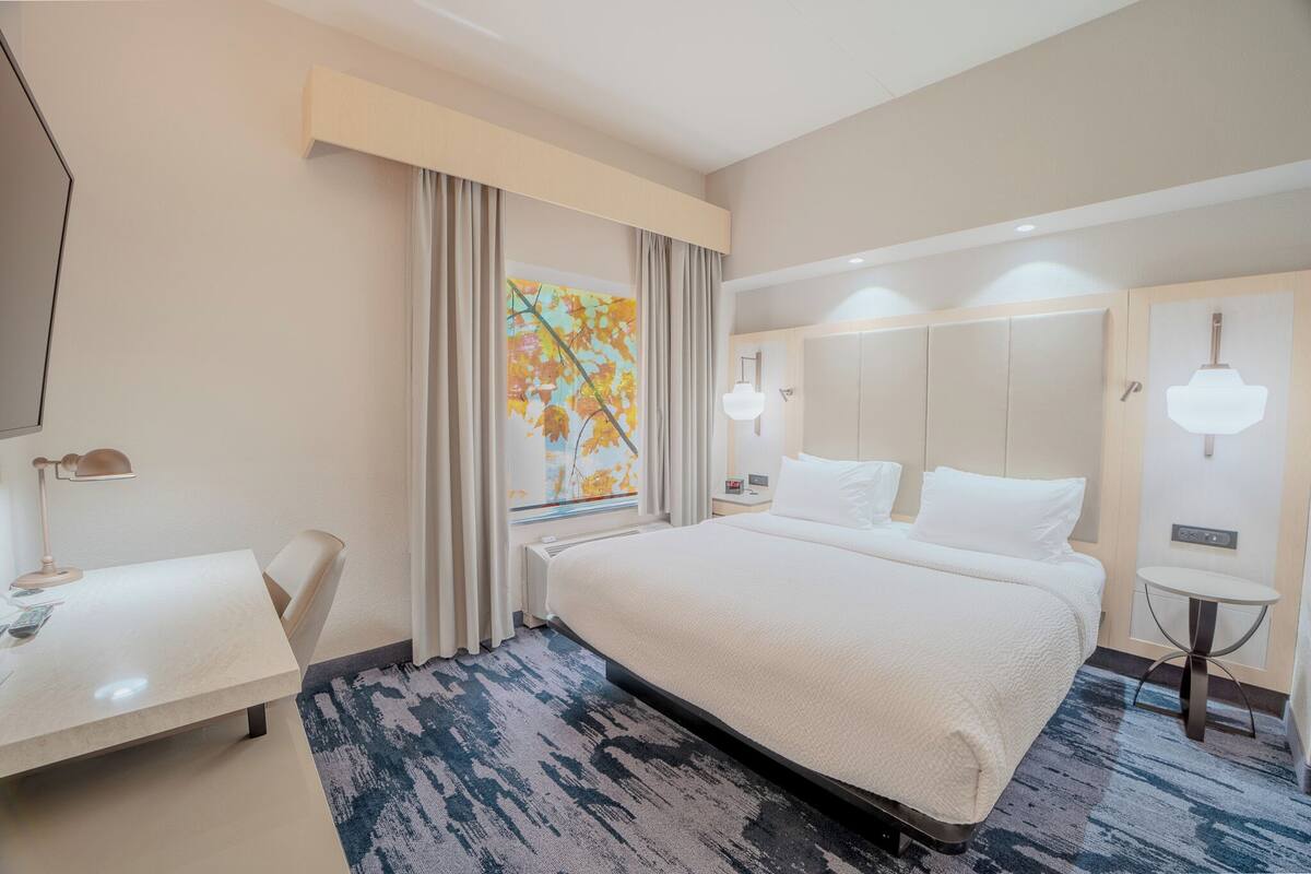 A hotel room with a large bed, a desk, a chair, a small table, and a window with curtains.