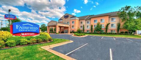 A Fairfield Inn & Suites by Marriott hotel with a parking lot and a clear sky.