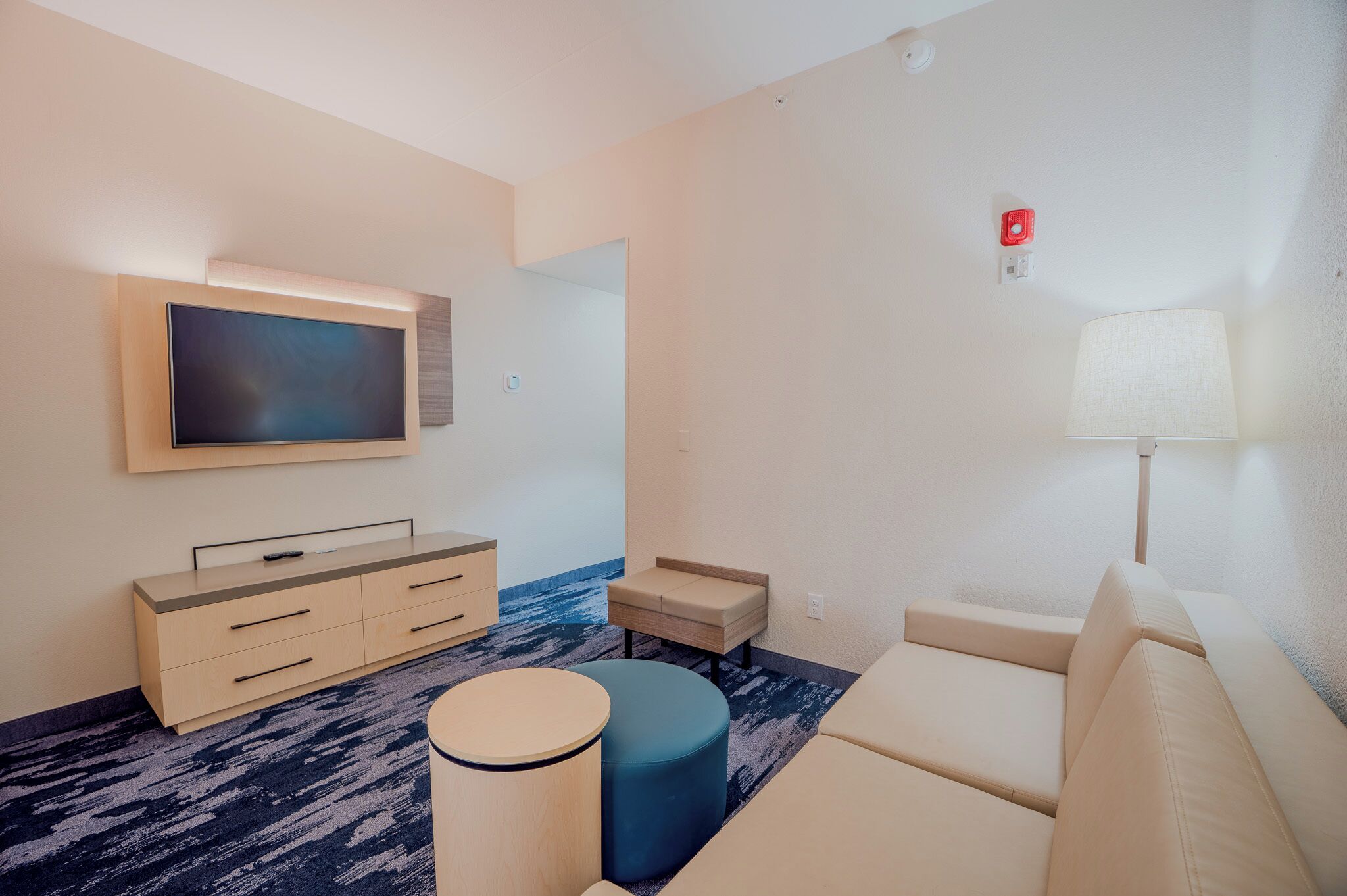 A modern hotel room with a flat-screen TV, a sofa, a small round table, and a lamp.