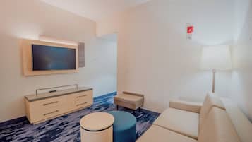 Une chambre d’hôtel moderne équipée d’un téléviseur à écran plat, d’un canapé, d’une petite table ronde et d’une lampe.