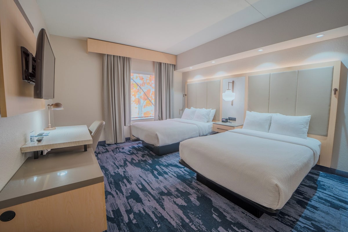 A hotel room with two beds, a desk, a TV, and a window with curtains.