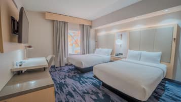 Une chambre d’hôtel avec deux lits, un bureau, une télévision et une fenêtre avec des rideaux.